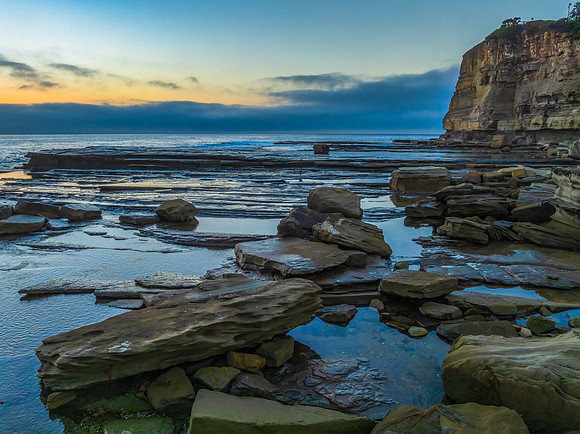 Sunrise seascape and rocky Inlet with thick fog cloud over the o