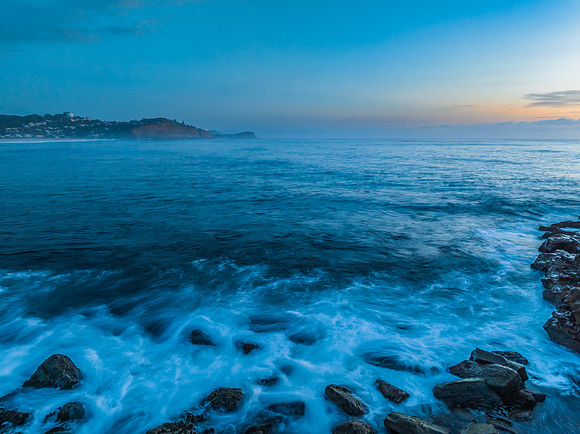 Sunrise over the calm ocean with light cloud and rocks