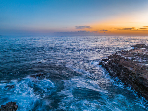 Sunrise over the calm ocean with light cloud and rocks