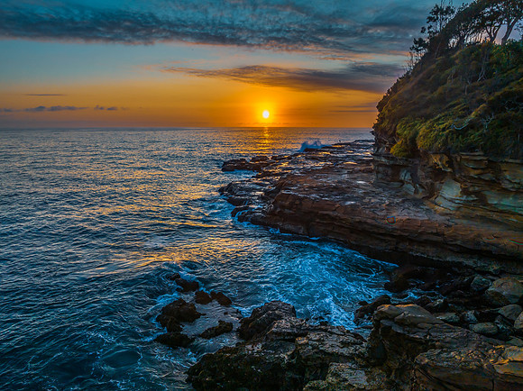 Sunrise over the calm ocean with light cloud and rocks
