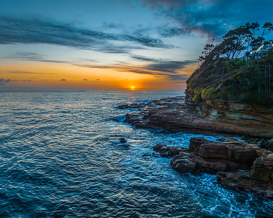 Sunrise over the calm ocean with light cloud and rocks