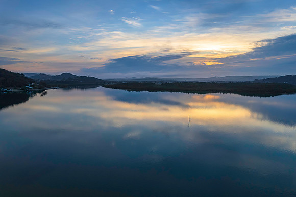 Soft and peaceful sunrise aerial waterscape with clouds and refl