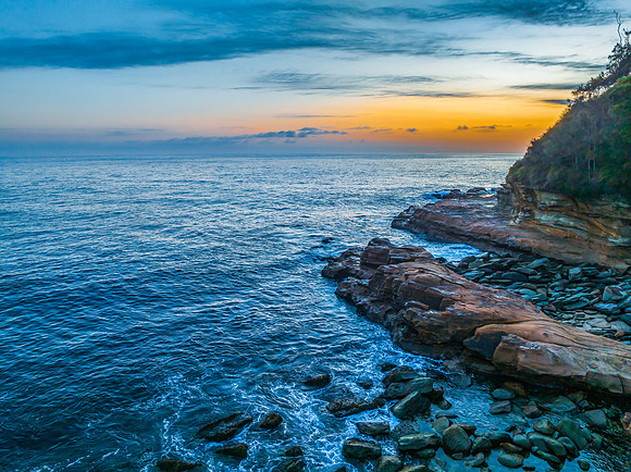 Sunrise over the calm ocean with light cloud and rocks