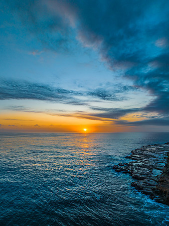 Sunrise over the calm ocean with light cloud and rocks