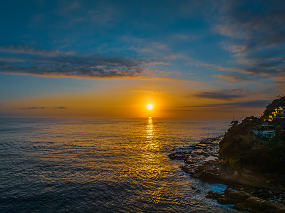 Sunrise over the calm ocean with light cloud and rocks