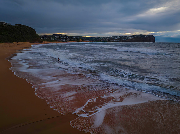 Winter sunrise seascape with rain clouds and lone swimmer