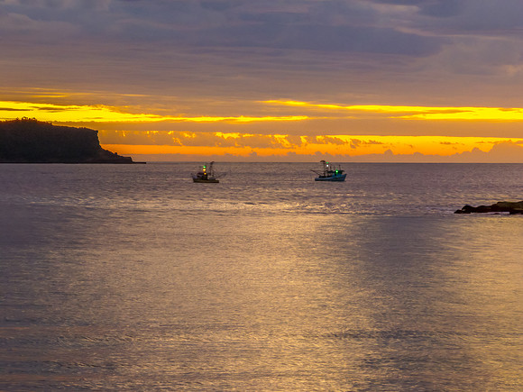 Sunrise over the ocean with clouds, fishing boats and a calm sea
