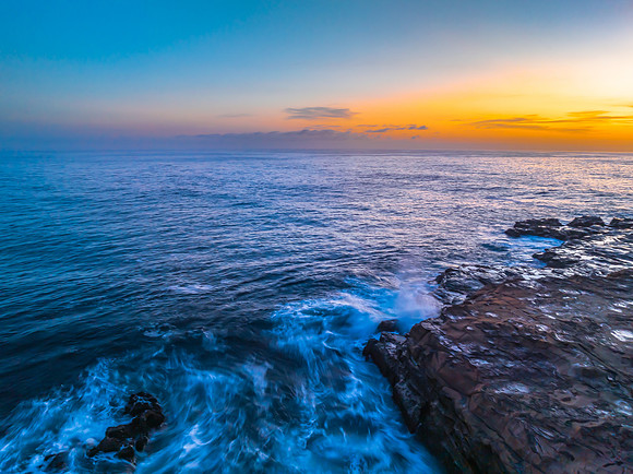 Sunrise over the calm ocean with light cloud and rocks