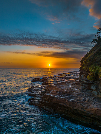 Sunrise over the calm ocean with light cloud and rocks