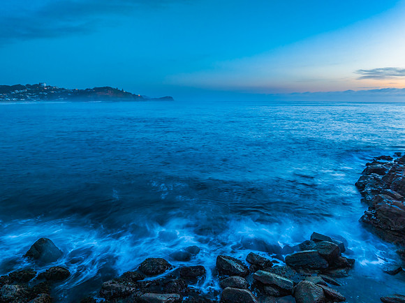 Sunrise over the calm ocean with light cloud and rocks