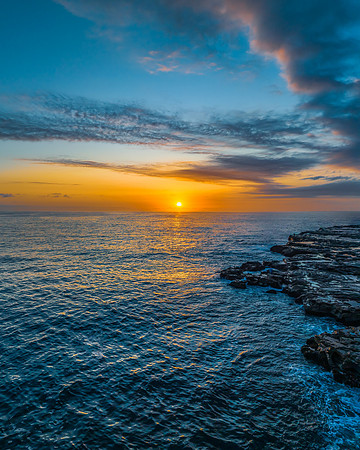 Sunrise over the calm ocean with light cloud and rocks