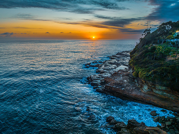Sunrise over the calm ocean with light cloud and rocks