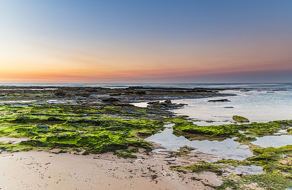 Green mossy rocks and beach sunrise seascape