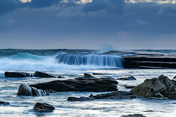 Moody sunrise seascape with clouds and casscades over the rock p