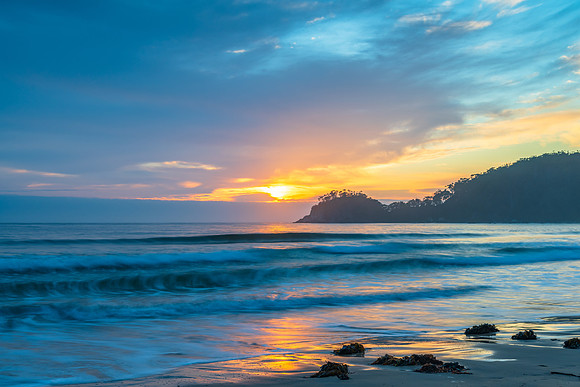 Sunrise at the seaside with cloud cover and seaweed
