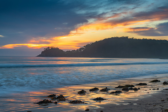 Sunrise at the seaside with cloud cover and seaweed