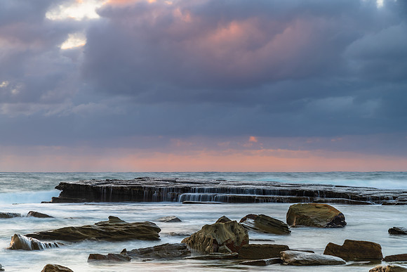 Moody sunrise seascape with clouds and casscades over the rock p