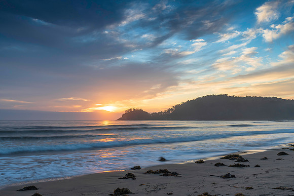 Sunrise at the seaside with cloud cover and seaweed
