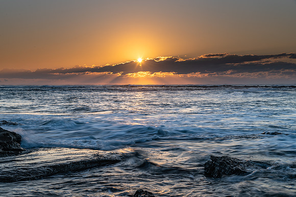 Sunrise Seascape with a sunburt through the low cloud bank and rock platform