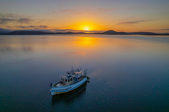Sunrise waterscape with a boat, soft clouds and golden glow
