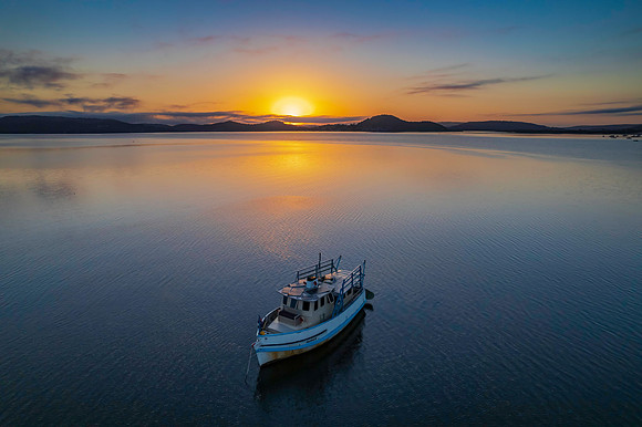 Sunrise waterscape with a boat, soft clouds and golden glow