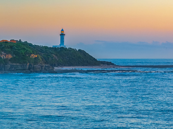 Sunrise over the sea and rocks with clear skies and lighthouse