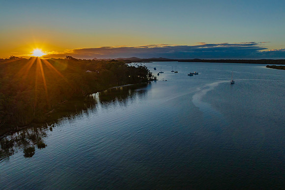 Sunrise over the river with boats and a sunburst