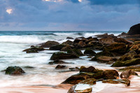 Sunrise at the seaside with rocks and rain clouds
