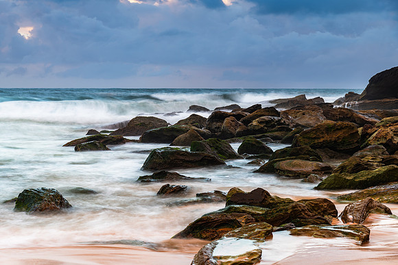 Sunrise at the seaside with rocks and rain clouds