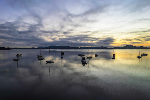 Sunrise waterscape with boats, soft clouds and reflections
