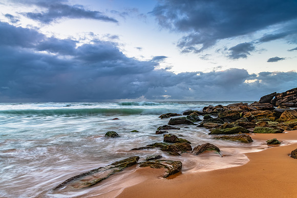 Sunrise at the seaside with rocks and rain clouds