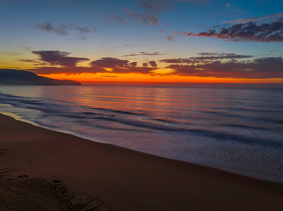 Orange dawn breaks over the ocean with small waves and clouds