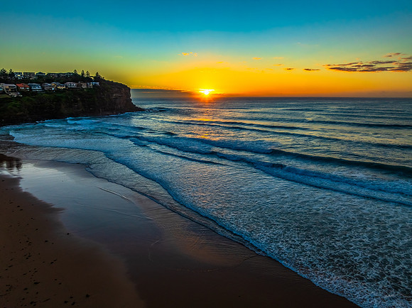 Sunrise at the beach with waves and a smattering of clouds