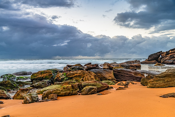 Sunrise at the seaside with rocks and rain clouds