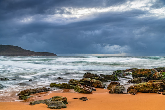 Sunrise at the seaside with rocks and rain clouds
