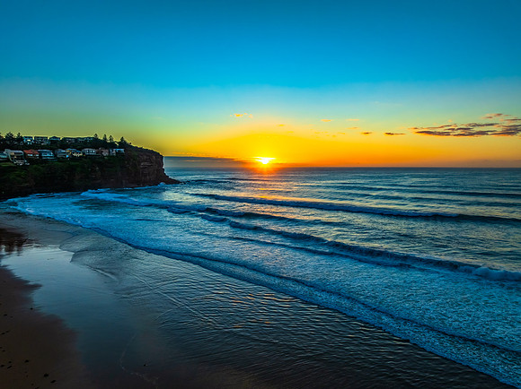 Sunrise at the beach with waves and a smattering of clouds