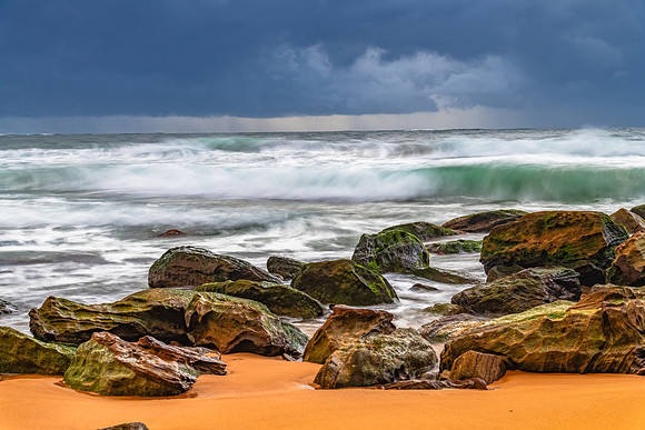Sunrise at the seaside with rocks and rain clouds