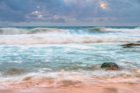 Sunrise at the seaside with rocks and rain clouds