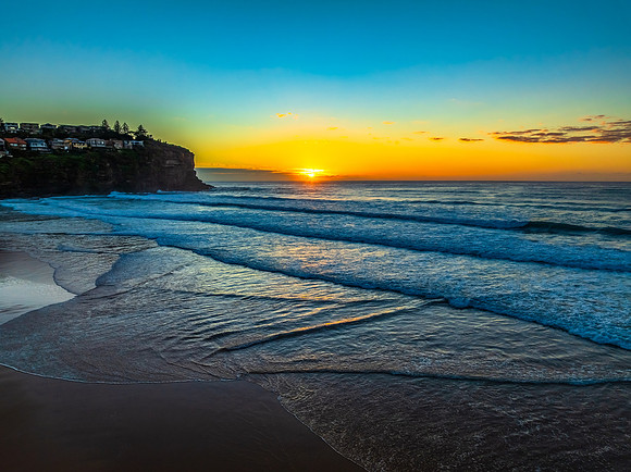 Sunrise at the beach with waves and a smattering of clouds