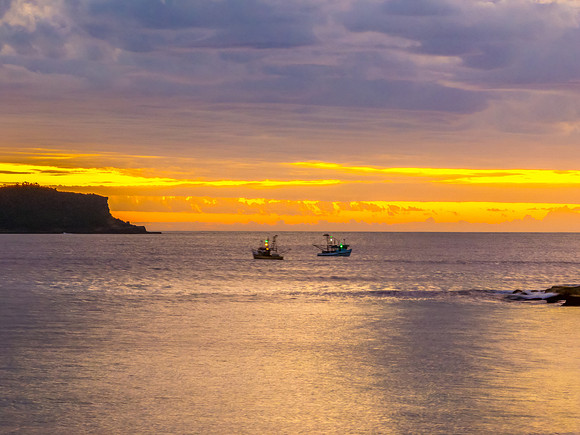 Sunrise over the ocean with clouds, fishing boats and a calm sea