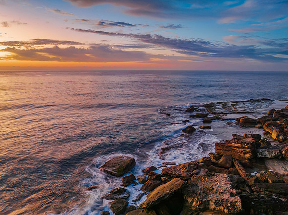 Peaceful sunrise over the ocean with small waves and clouds