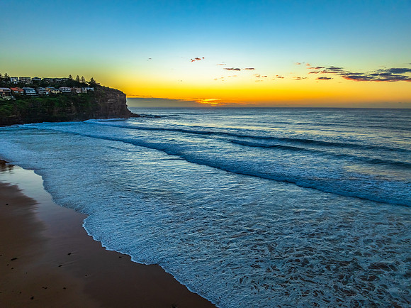 Sunrise at the beach with waves and a smattering of clouds