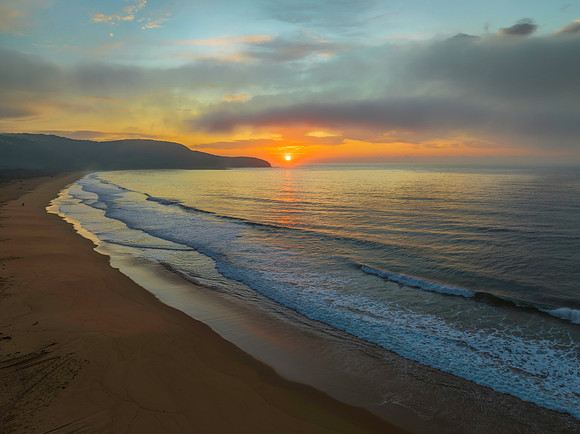 Peaceful sunrise over the ocean with small waves and clouds