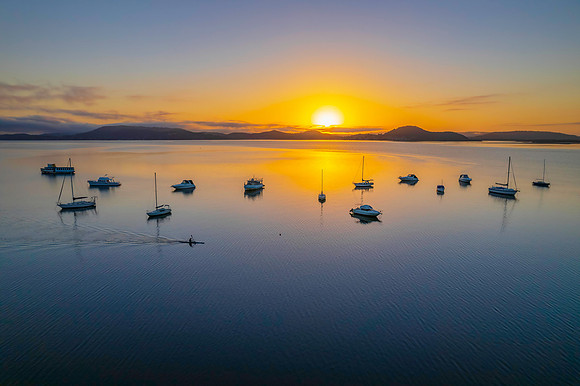 Sunrise waterscape with boats, soft clouds and reflections