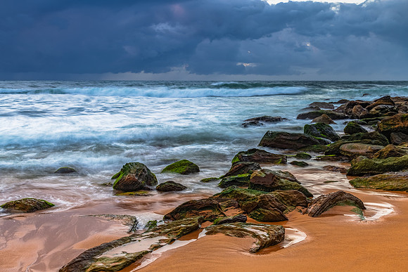 Sunrise at the seaside with rocks and rain clouds