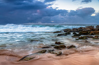 Sunrise at the seaside with rocks and rain clouds