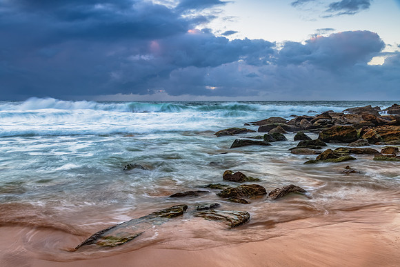 Sunrise at the seaside with rocks and rain clouds