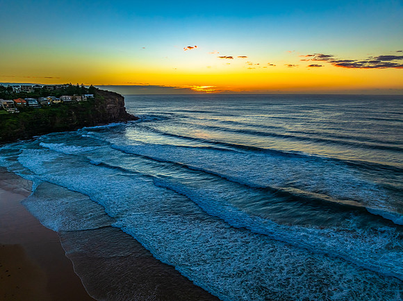 Sunrise at the beach with waves and a smattering of clouds