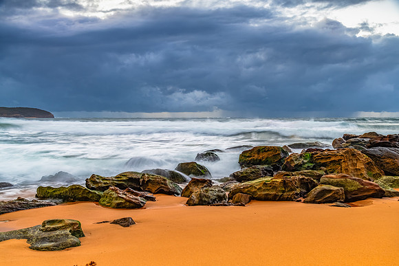 Sunrise at the seaside with rocks and rain clouds