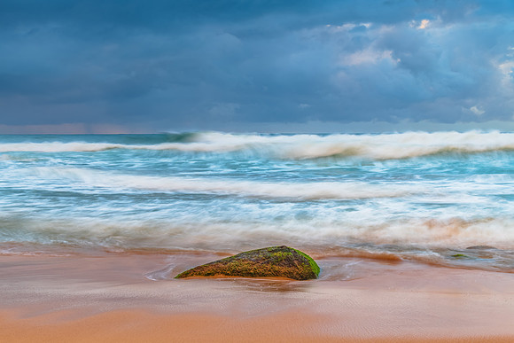 Sunrise at the seaside with rocks and rain clouds